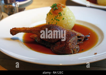 Vicino la porzione di confit di anatra gamba con gnocco di patate palla e birra salsa, piatto tradizionale bavarese la cucina tedesca, sulla piastra bianca su tavola, hi Foto Stock