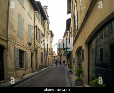 Strada stretta in Arles città situata in Francia. Vista della facciata medievale con vecchie porte e finestre. Tre uomini stanno camminando insieme nel piccolo vicolo. Foto Stock