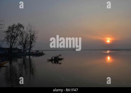 Srinagar, India. Il 30 dicembre 2018. Un barcaiolo visto il canottaggio la sua barca shikara sulle acque di Dal lago durante una fredda sera a Srinagar, Indiano Kashmir amministrato.La notte le temperature in Kashmir è salito da diversi gradi a causa di un cielo nuvoloso, fornendo un enorme sollievo per i residenti dalla intensa ondata di freddo.Tuttavia, le temperature hanno continuato a stabilirsi al di sotto del punto di congelamento. Srinagar ha registrato un minimo di meno di 2,4 gradi Celsius durante la notte per un incremento di quasi cinque gradi da meno 7,2 gradi Celsius. Credito: Saqib Majeed SOPA/images/ZUMA filo/Alamy Live News Foto Stock