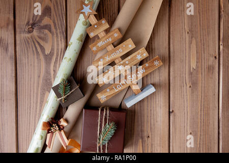 Avvolgere i regali di Natale nel mestiere di carta sul tavolo di legno. Procedimento di avvolgimento di doni. Sfondo di stile di vita. Vista da sopra. Concetto di natale. Foto Stock