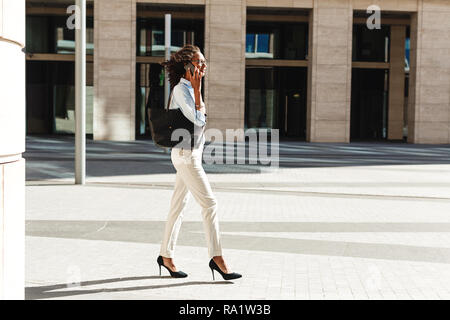 Vista laterale del giovane imprenditrice a piedi nella parte anteriore di un edificio di moderna costruzione Foto Stock