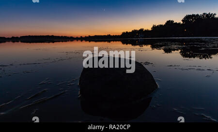 Una pietra solitario siede nella riflessione del Cielo di tramonto. Foto Stock