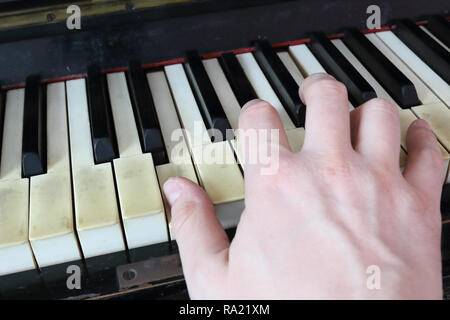 Una mano destra giocando a E (MI) principali corda su un vecchio nero pianoforte con ingiallito Tasti rotti, premendo il tasto E (MI), G# diesis (SOL#), B (SI) note Foto Stock