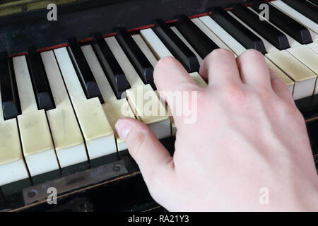 Una mano destra giocando una G (SOL) principali corda su un vecchio nero pianoforte con ingiallito Tasti rotti, premendo il tasto G (SOL), B (SI), D (RI) note Foto Stock