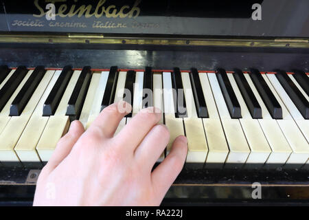 Una mano destra giocando a E (MI) principali corda su un vecchio nero pianoforte con ingiallito Tasti rotti, premendo il tasto E (MI), G# diesis (SOL#), B (SI) note Foto Stock