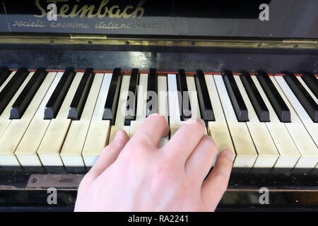 Una mano destra giocando una G (SOL) principali corda su un vecchio nero pianoforte con ingiallito Tasti rotti, premendo il tasto G (SOL), B (SI), D (RI) note Foto Stock