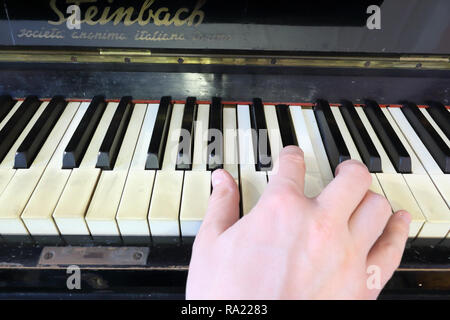 Una mano destra giocando a B (SI) principali corda su un vecchio nero pianoforte con ingiallito tasti incrinato, con la B (SI), D# diesis (RE#), F# diesis (FA#) note Foto Stock