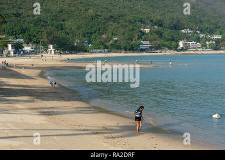 Beachcombers esaminare la riva del mare lungo Mui Wo beach sull'Isola di Lantau, Hong Kong Foto Stock