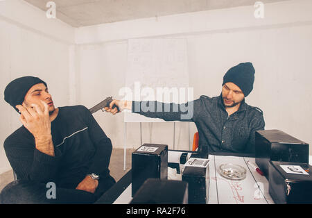 Due criminali sono seduto in una stanza e sostenendo tenendo in mano una pistola appuntita Foto Stock