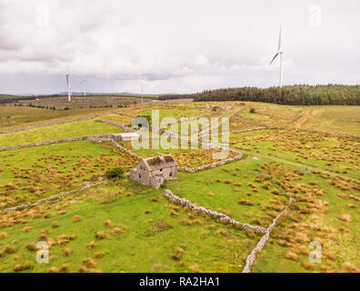 Una veduta aerea di turbine eoliche e un'azienda abbandonata casa tra le città di Spiddal e Moycullen nella Contea di Galway, Irlanda Foto Stock