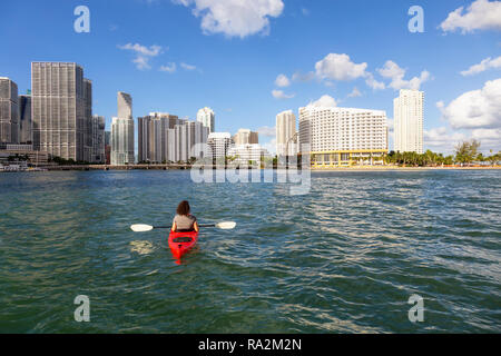 Ragazza avventurosa kayak nella parte anteriore di un moderno centro di Cityscape durante una serata di sole. Prese a Miami, Florida, Stati Uniti d'America. Foto Stock