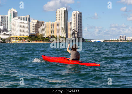 Ragazza avventurosa kayak nella parte anteriore di un moderno centro di Cityscape durante una serata di sole. Prese a Miami, Florida, Stati Uniti d'America. Foto Stock