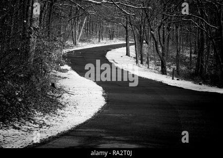 Una strada di campagna in salita curve circondato dalla neve in inverno, in bianco e nero Foto Stock