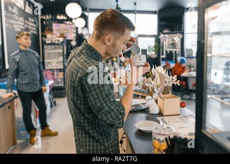 Moderna caffetteria, lavorando il caffè barista, persone seduti ai tavoli, luce diurna, inverno interiore. Foto Stock