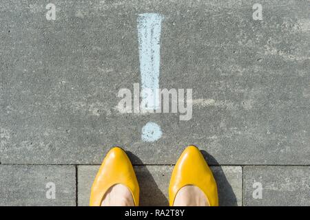 I piedi femminili con punto esclamativo, simbolo di attenzione tracciata sull'asfalto. Foto Stock