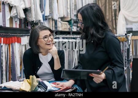 Due donne che lavorano con i tessuti interni digitale compressa in showroom per tende e tessuti di rivestimento, designer e acquirente la scelta di tessuti in new int Foto Stock