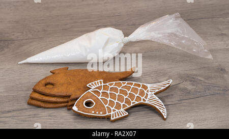 Dolce natalizio e sacchetto di glassa impilati su uno sfondo di legno. Close-up di tradizionale Xmas nad Anno Nuovo gingerbreads in forma di pesce. Preparare per la decorazione. Foto Stock