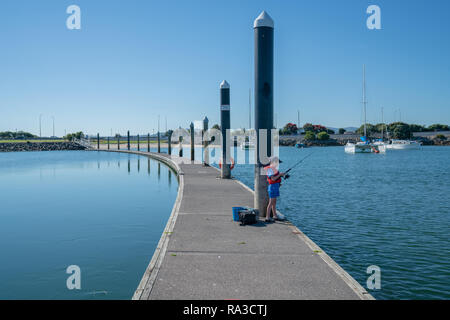 Piccolo Ragazzo sul molo di immagine di divisione e di calma da acque torbide in rosso la vita giacca pesca dal molo della marina sul soleggiato al mattino calmo Foto Stock