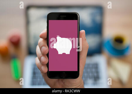 Un uomo guarda al suo iPhone che visualizza il logo Piggybank (solo uso editoriale). Foto Stock