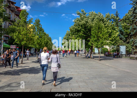 A Pristina, Kosovo - 30 Maggio 2018 - un grande gruppo di persone che camminano in un ampio marciapiede con grandi alberi verdi e cielo blu a Pristina, capitale del Kosovo Foto Stock