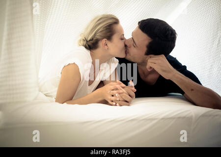 Coppia caucasica baciare sotto le lenzuola del letto di casa in camera da letto - intimo stile di vita per i giovani in amore - Romantico San Valentino c Foto Stock