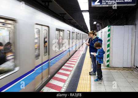 Western madre e figlio i viaggiatori in attesa in metropolitana per il passaggio di un treno, Tokyo Foto Stock