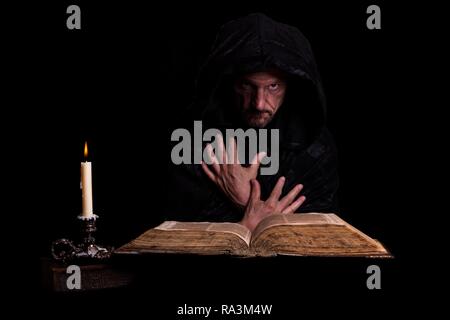 L'uomo, nero con un cappotto con cappuccio, davanti una candela che brucia e un vecchio libro, Germania Foto Stock