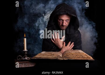 L'uomo, nero con un cappotto con cappuccio, davanti una candela che brucia e un vecchio libro, Germania Foto Stock