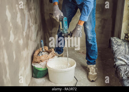 Giovane maschio pittore massaggia putty con acqua in un secchio con un hand-held mixer per mix di costruzione Foto Stock