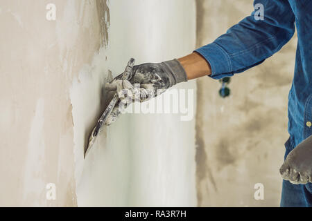 Master è l'applicazione di stucco bianco su una parete e macchie da coltello da stucco in una stanza per restauro di casa in ore diurne Foto Stock