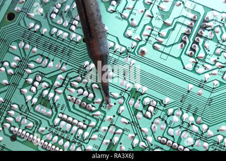 Un saldatore a punta placcato saldatura un foro passante il componente sulla sua via su una verde scheda a circuito stampato Foto Stock