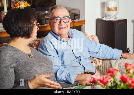 Felice di anziani giovane seduto sul divano in un disegno floreale in casa Foto Stock