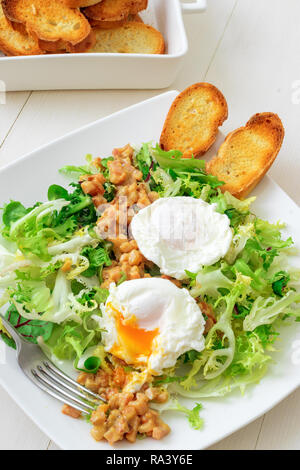 Classica insalata francese, grande insalata Lyonnaise. Il piatto con il verde delle foglie di lattuga, Digione la salsa di senape con pezzi di pancetta fritta e grigliate di pane francese, Foto Stock