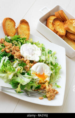 Classica insalata francese, grande insalata Lyonnaise. Il piatto con il verde delle foglie di lattuga, Digione la salsa di senape con pezzi di pancetta fritta e grigliate di pane francese, Foto Stock