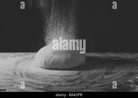 La pasta in forma di una scodella giace su una tavola di legno tabella di cottura al buio su un sfondo nero. Cosparsa di farina. Vista laterale, la foto in orizzontale Foto Stock