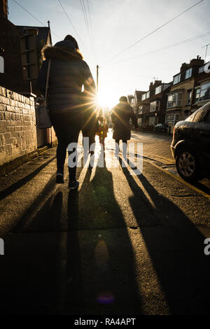 Famiglia camminare per la strada in un balneare inglese verso la luce del sole Foto Stock