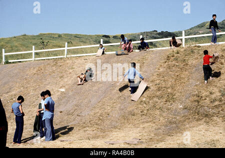 1975 - Bambini scorrere su una collina a una temporanea struttura alloggiativa per rifugiati vietnamiti. Foto Stock