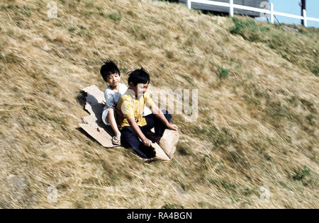 1975 - Bambini scorrere su una collina a una temporanea struttura alloggiativa per rifugiati vietnamiti. Foto Stock