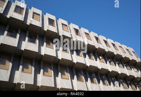 I piani superiori e vetri colorati di bassa altezza in cemento blocco ufficio in croce illuminata dalla luce del sole con cielo blu dietro. Foto Stock