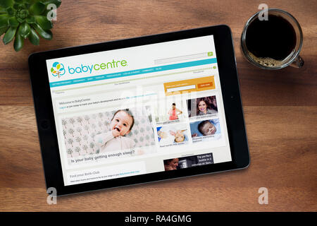 Il sito web di BabyCenter è visto su un tablet iPad, su di un tavolo di legno lungo con un caffè espresso e una pianta di casa (solo uso editoriale). Foto Stock