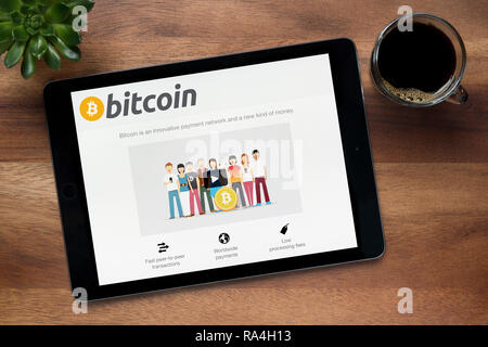 Il sito web di Bitcoin.org è visto su un tablet iPad, su di un tavolo di legno lungo con un caffè espresso e una pianta di casa (solo uso editoriale). Foto Stock