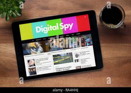 Il sito web di Digital Spy è visto su un tablet iPad, su di un tavolo di legno lungo con un caffè espresso e una pianta di casa (solo uso editoriale). Foto Stock