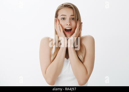 Vita-up shot di interessati caucasico carina ragazza con i capelli biondi urlando di paura in bocca aperta guardando preoccupato, afferrando il viso con le mani fissando in questione e in preda al panico come non avendo nulla di usura in armadio Foto Stock