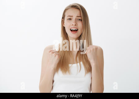 Ragazza desperatly cheers per amico mettendo sforzo per gridare parole di sostegno che guardano con speranza alla telecamera a bocca aperta e accigliata, stringendo i pugni in segno di vittoria e tirumph attesa per punteggio finale Foto Stock