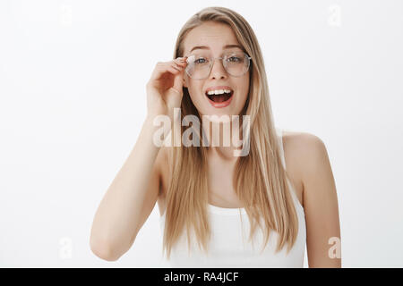 Ragazza mettendo su vetri di essere rimasto sorpreso e felice di vedere volto familiare nella massa, sospiri sollevato e stupiti toccando di RIM di eyewear rendendo impressionato e gioioso gesto su sfondo grigio Foto Stock