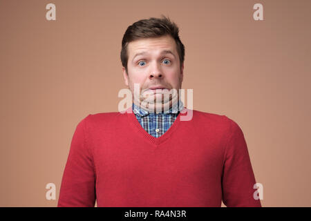 Oops. Funny uomo caucasico in maglione rosso smorfie colpevole di fronte a sfondo per studio Foto Stock