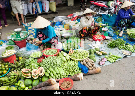Donne vietnamita stallholders indossando cappelli conici visualizzazione di frutta fresca locale e ortaggi per la vendita in un mercato. Can Tho Mekong Delta Vietnam Asia Foto Stock