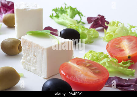 Insalata greca, bianco formaggio greco, verde e olive nere, le foglie di lattuga, halfs di pomodoro ciliegino. Sfondo bianco. variazioni di foglie di insalata e formaggio feta Foto Stock