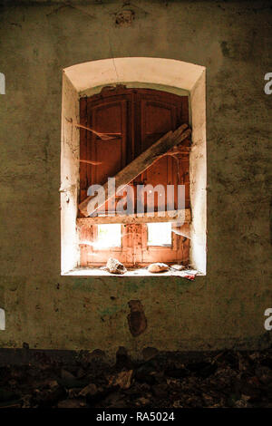 Finestra di una casa abbandonata dall'interno; la luce illumina la stanza un po', lasciando intravedere le ragnatele e la parete di pelatura Foto Stock