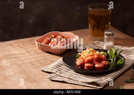 Bicchiere di birra deliziosa con salsicce alla griglia su un tavolo di legno Foto Stock